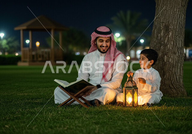 تلاوة وحفظ القرآن الكريم، زينة وفانوس شهر رمضان المبارك، جلسة خارجية في الهواء الطلق، تربية الاولاد على الفطرة الاسلامية الصحيحة، رجل عربي خليجي سعودي يرتدي الشماغ والثوب التقليدي يجلس على العشب يقرأ من المصحف الشريف بجانب ابنه في الليل
