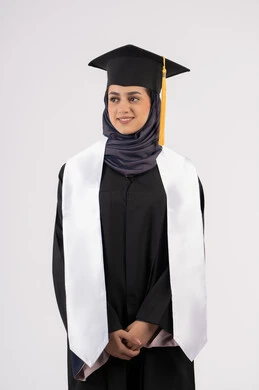 الوقوف باستقامة والتقاط  صور شخصية بثياب التخرج، بورتريه لإمرأة عربية خليجية سعودية مبتسمة ترتدي القبعة وعباءة التخرج تنظر الى شيء ما بتعابير السرور والسعادة، خريجة اماراتية تحتفل بإنهاء المرحلة الجامعية، مفهوم التفوق والنجاح والاجتهاد، خلفية بيضاء