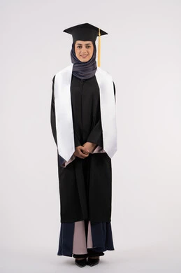 التقاط صور شخصية بثياب التخرج، بورتريه لإمرأة عربية خليجية سعودية مبتسمة ترتدي القبعة وعباءة التخرج تنظر الى الكاميرا بتعابير السرور والسعادة، خريجة اماراتية تحتفل بإنهاء المرحلة الجامعية، مفهوم التفوق والنجاح والاجتهاد، الجسم بالطول الكامل، خلفية بيضاء