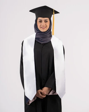 خريجة اماراتية تحتفل بإنهاء المرحلة الجامعية، الوقوف باستقامة والتقاط  صور شخصية بثياب التخرج، بورتريه لإمرأة عربية خليجية سعودية مبتسمة ترتدي القبعة وعباءة التخرج تنظر الى الكاميرا بتعابير السرور والسعادة، مفهوم التفوق والنجاح والاجتهاد، خلفية بيضاء