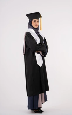 تعابير السرور والثقة بالنفس، خريجة اماراتية تقف بأيدي متقاطعة وتقوم بالتقاط  صور شخصية بثياب التخرج، بورتريه لإمرأة عربية خليجية سعودية مبتسمة ترتدي القبعة وعباءة التخرج تحتفل بإنهاء المرحلة الجامعية، التفوق والنجاح والاجتهاد، الجسم بالطول الكامل، خلفية بيضاء