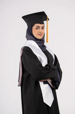 الاحتفال بإنهاء المرحلة الجامعية، خريجة اماراتية تقف بأيدي متقاطعة وتقوم بالتقاط  صور شخصية بثياب التخرج، بورتريه لإمرأة عربية خليجية سعودية مبتسمة ترتدي القبعة وعباءة التخرج  بتعابير السرور والثقة بالنفس، مفهوم التفوق والنجاح والاجتهاد، خلفية بيضاء