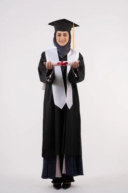 The concept of success and excellence, a young Saudi woman looking at the camera with gestures of pride, gestures of happiness for achieving her dream, a university occasion and celebration, a celebration of completing university studies, a portrait of a veiled Arab Gulf Emirati graduate wearing a graduation gown and cap, holding a certificate in her hand, white background