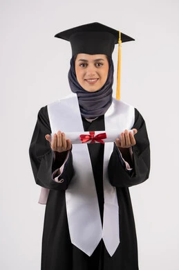 A young Saudi woman looking at the camera with gestures of pride, the concept of success and excellence, gestures of happiness at achieving a dream, a university occasion and celebration, celebrating the completion of university studies, a portrait of a veiled Arab Gulf Emirati graduate wearing a graduation gown and cap, holding a certificate in her hand, white background