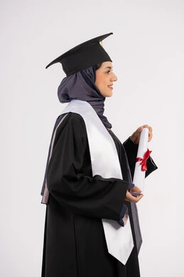 مناسبة واحتفال جامعي، شابة سعودية تنظر الى مكان ما بايماءات الفخر، تعابير السعادة بالوصول الى الحلم، مفهوم النجاح والتفوق، الاحتفال بإنهاء الدراسة الجامعية، بورتريه من الجانب لخريجة عربية خليجية اماراتية محجبة ترتدي زي التخرج والقبعة تحمل بيدها الشهادة، خلفية بيضاء