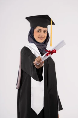 تعابير السعادة بالوصول الى الحلم، شابة سعودية تنظر الى الكاميرا بايماءات الفخر، مفهوم النجاح والتفوق، مناسبة واحتفال جامعي، الاحتفال بإنهاء الدراسة الجامعية، بورتريه لخريجة عربية خليجية اماراتية محجبة ترتدي زي التخرج والقبعة تحمل بيدها الشهادة، خلفية بيضاء