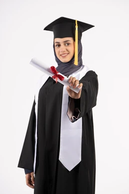 Expressions of happiness at achieving a dream, a young Saudi woman looking at the camera with gestures of pride, the concept of success and excellence, a university occasion and celebration, a celebration of completing university studies, a portrait of a veiled Arab Gulf Emirati graduate wearing a graduation gown and cap, holding a certificate in her hand, white background