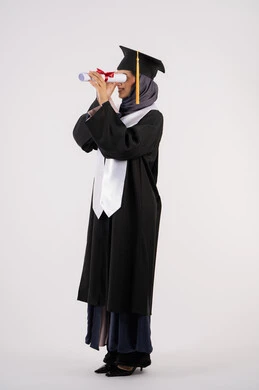 التطلع الى المستقبل بعد التخرج، بورتريه من الجانب لشابة عربية خليجية سعودية مبتسمة ترتدي القبعة وزي التخرج تمسك الشهادة كالمنظار، خريجة اماراتية تحتفل بانتهاء مرحلة الدراسة الجامعية، النجاح والتفوق والاجتهاد، الجسم بالطول الكامل، خلفية بيضاء