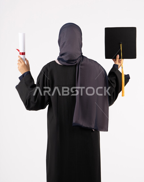 الوصول للحلم والنجاح، انتهاء مرحلة الدراسة الجامعية، التفوق والاجتهاد والجد، بورتريه من الخلف لشابة عربية خليجية سعودية محجبة ترتدي زي التخرج تمسك بيدها الشهادة والقبعة، خريجة اماراتية تحتفل بتخرجها من الجامعة، خلفية بيضاء