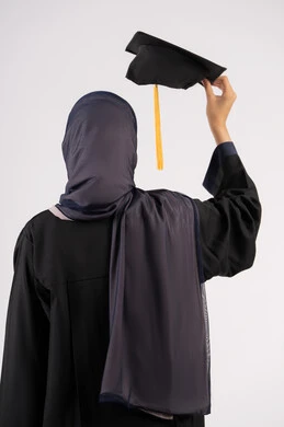 الوصول للحلم والنجاح، انتهاء مرحلة الدراسة الجامعية، التفوق والاجتهاد والجد، بورتريه مقرب من الخلف لشابة عربية خليجية سعودية محجبة ترتدي زي التخرج تمسك بيدها الشهادة والقبعة، خريجة اماراتية تحتفل بتخرجها من الجامعة، خلفية بيضاء