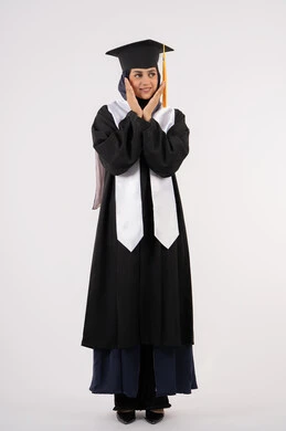 Gestures and expressions of pleasure and happiness, looking at a place, portrait of a smiling young Saudi Arabian Gulf woman wearing a graduation cap and gown, placing her hands under her face with feminine gestures, celebrating university graduation, Emirati graduate finishing university studies, full body, white background