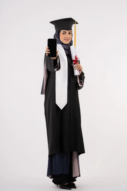 Online study applications, displaying a blank black screen on a mobile phone, portrait of a young Saudi Arabian Gulf Arab woman wearing a cap and graduation gown holding a diploma, a smiling Emirati graduate standing with an expression of pleasure and happiness, celebrating the end of the university stage, full body, white background
