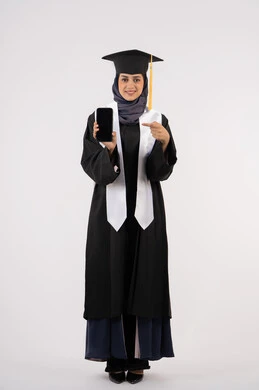 Pointing to a blank black screen on a mobile phone, portrait of a young Saudi Arabian Gulf Arab woman wearing a cap and graduation gown looking at the camera, Emirati graduate standing with an expression of pleasure and happiness, online study applications, celebrating the end of the university stage, full body, white background