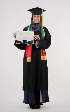 Looking at the camera with gestures of pride, success, excellence and graduation from university, gestures of happiness for achieving the dream, university occasion and celebration, celebration of completing university studies, portrait of a veiled Arab Gulf Emirati female graduate wearing graduation attire and cap holding the certificate in her hand, white background