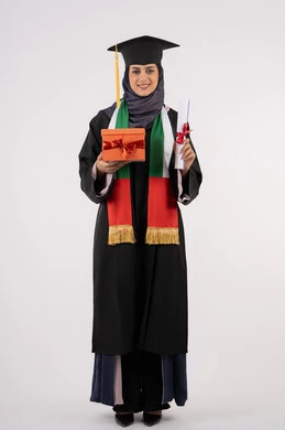 Celebrating the completion of university studies, the concept of diligence and excellence, expressions of happiness at achieving the dream of success, giving gifts on occasions, a university occasion and celebration, a portrait of a veiled Arab Gulf Emirati graduate wearing a graduation gown and cap, holding a gift box with a certificate, white background
