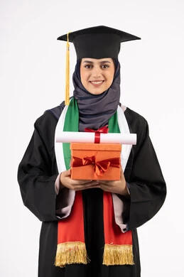 The concept of diligence and excellence, expressions of happiness at achieving the dream of success, celebrating the completion of university studies, giving gifts on occasions, a university occasion and celebration, a portrait of a veiled Arab Gulf Emirati graduate wearing a graduation gown and cap, holding a gift box with a certificate, white background