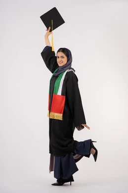 المناسبات والاحتفالات الجامعية، النظر الى الكاميرا بايماءات الفخر، الوصول إلى حلم النجاح، مفهوم الاجتهاد والتفوق، الاحتفال بإنهاء الدراسة الجامعية، مناسبة واحتفال جامعي، بورتريه لخريجة عربية خليجية اماراتية محجبة ترتدي زي التخرج تمسك بيدها القبعة، خلفية بيضاء