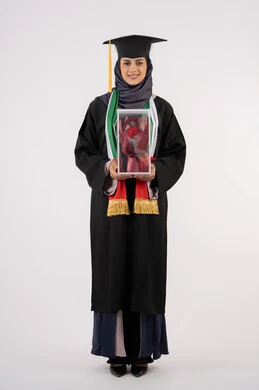 University occasion and celebration, celebration of completing university studies, gestures of happiness for reaching the dream of success, portrait of a veiled Arab Gulf Emirati graduate wearing graduation dress and cap, holding a bouquet of flowers in her hand, looking at the camera with an expression of pleasure, full body, white background