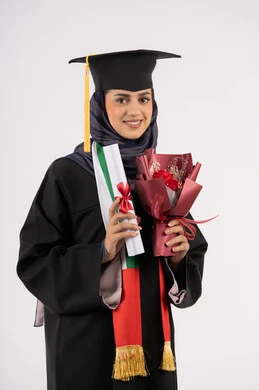 احتفال ومناسبة جامعية، الاحتفال بإنهاء الدراسة الجامعية، إيماءات السعادة بالوصول لحلم النجاح، مفهوم الاجتهاد والتفوق، النظر إلى الكاميرا بتعابير السرور، بورتريه لخريجة عربية خليجية اماراتية محجبة ترتدي زي التخرج والقبعة تمسك بيدها باقة ورد والشهادة، خلفية بيضاء