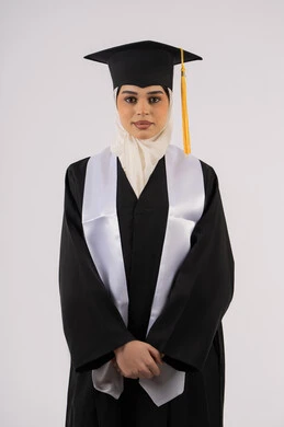 مفهوم التفوق والنجاح والاجتهاد، خريجة اماراتية تحتفل بإنهاء المرحلة الجامعية، الوقوف باستقامة والتقاط  صور شخصية بثياب التخرج، بورتريه لشابة عربية خليجية سعودية مبتسمة ترتدي القبعة وعباءة التخرج تنظر الى الكاميرا بتعابير السرور، خلفية بيضاء