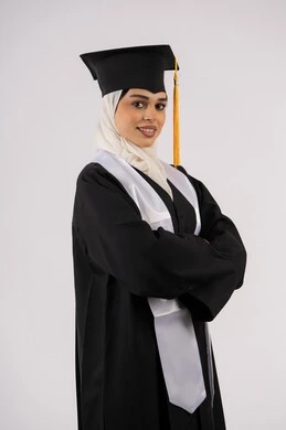 التقاط  صور شخصية بثياب التخرج، خريجة اماراتية تحتفل بإنهاء المرحلة الجامعية، بورتريه لشابة عربية خليجية سعودية مبتسمة ترتدي القبعة وعباءة التخرج تقف بأيدي متقاطعة وتنظر الى الكاميرا بتعابير السرور، مفهوم التفوق والنجاح والاجتهاد، خلفية بيضاء