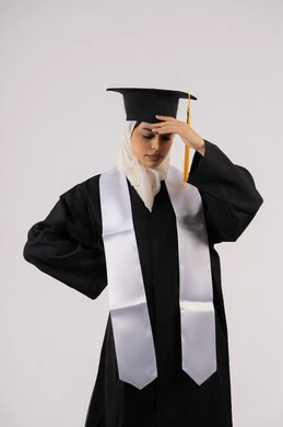 الانتهاء من مرحلة الدراسة الجامعية بعد عناء، الارهاق والتعب بعد الاجتهاد والمثابرة، بورتريه لشابة عربية خليجية اماراتية ترتدي القبعة وزي التخرج تضع يدها على رأسها بتعابير اليأس، خريجة اماراتية تنتظر نتائجها، خلفية بيضاء