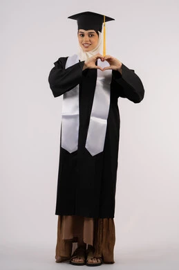 ايماءات يدين على شكل قلب، التعبير عن الحب والفرح، التقاط  صور شخصية بثياب التخرج، خريجة اماراتية تحتفل بإنهاء المرحلة الجامعية، بورتريه لشابة عربية خليجية سعودية مبتسمة ترتدي القبعة وعباءة التخرج تنظر الى الكاميرا بتعابير السرور، صورة الجسم بالكامل، خلفية بيضاء