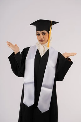 مفهوم التفوق والنجاح، تعابير الأنوثة واللطافة، التقاط  صور شخصية بثياب التخرج، خريجة اماراتية تحتفل بإنهاء المرحلة الجامعية، بورتريه لشابة عربية خليجية سعودية مبتسمة ترتدي القبعة وعباءة التخرج تنظر الى الكاميرا بتعابير السرور، خلفية بيضاء