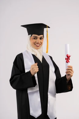 Pride in achieving dreams, raising a fist with an expression of achievement, looking at the camera with gestures of happiness and joy, a Saudi graduate celebrating the completion of university, a portrait of an Arab Gulf Emirati woman wearing a graduation cap and gown and holding a certificate, white background
