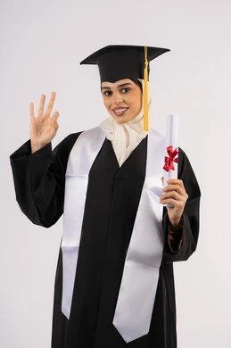 علامة الجودة والامتياز والتميز، الاحتفال بالوصول إلى الأحلام، خريجة سعودية تحتفل بإنهاء المرحلة الجامعية، بورتريه لامرأة عربية خليجية اماراتية ترتدي القبعة وعباءة التخرج وتحمل الشهادة تنظر إلى الكاميرا بإيماءات السعادة، خلفية بيضاء