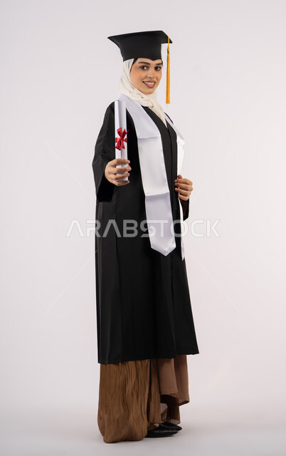 Looking at the camera with gestures of happiness and joy, celebrating reaching dreams, taking selfies in graduation gowns, Saudi graduate celebrating finishing university, portrait of an Emirati Gulf Arab woman wearing a graduation cap and gown and holding a certificate, full body photo, white background