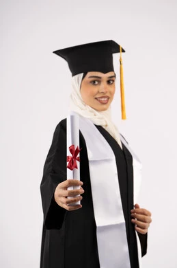 الاحتفال بالوصول إلى الأحلام، إظهار مشاعر الفرح بالتخرج، خريجة سعودية تحتفل بإنهاء المرحلة الجامعية، بورتريه من  الجانب لامرأة عربية خليجية اماراتية ترتدي القبعة وعباءة التخرج وتحمل الشهادة تنظر إلى الكاميرا بإيماءات السعادة، خلفية بيضاء