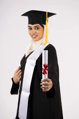 مشاعر الفرح بالتخرج، الاحتفال بالوصول إلى الأحلام، خريجة سعودية تحتفل بإنهاء المرحلة الجامعية، بورتريه من  الجانب لامرأة عربية خليجية اماراتية ترتدي القبعة وعباءة التخرج وتحمل الشهادة تنظر إلى الكاميرا بإيماءات السعادة، خلفية بيضاء