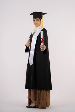 Showing feelings of joy at graduation, celebrating reaching dreams, Saudi female graduate celebrating finishing university, side portrait of an Emirati Gulf Arab woman wearing a graduation cap and gown and holding a certificate looking at the camera with happy gestures, full body portrait, white background