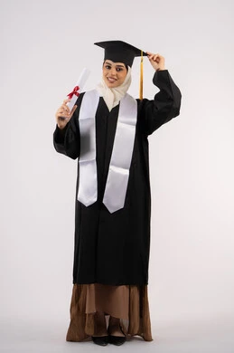 الفخر والفرح بالوصول لحلم التخرج, أهمية الدراسة الجامعية، بورتريه لخريجة عربية سعودية خليجية محجبة مبتسمة ترتدي ثياب التخرج وتحمل بيدها شهادة التفوق وتنظر إلى الكاميرا بإيماءات البهجة والسعادة، شابة إماراتية تحتفل بإنهاء دراستها، صورة لكامل الجسم، خلفية بيضاء