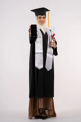 Online education and study applications, displaying a blank black screen on a mobile phone, a portrait of a young Saudi Arabian Gulf Arab woman wearing a cap and graduation gown holding a diploma in her hand, a smiling Emirati graduate standing with an expression of pleasure, celebrating the end of the university stage, full body, white background