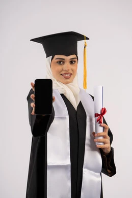 استخدام جهاز تقني حديث، عرض شاشة سوداء فارغة على الهاتف المحمول، تطبيقات الدراسة اونلاين، بورتريه لشابة عربية خليجية سعودية ترتدي القبعة وزي التخرج تمسك بيدها الشهادة، خريجة اماراتية مبتسمة تقف بتعابير السرور، الاحتفال بانتهاء المرحلة الجامعية، خلفية بيضاء