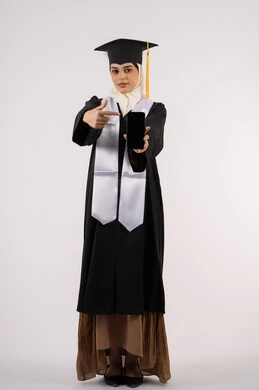 الإشارة باصبع السبابة إلى جهاز تقني حديث، عرض شاشة سوداء فارغة على الهاتف المحمول، بورتريه لشابة عربية خليجية سعودية ترتدي زي التخرج تمسك بيدها الشهادة، خريجة اماراتية مبتسمة تقف بتعابير السرور، الاحتفال بانتهاء المرحلة الجامعية، الجسم بالطول الكامل، خلفية بيضاء