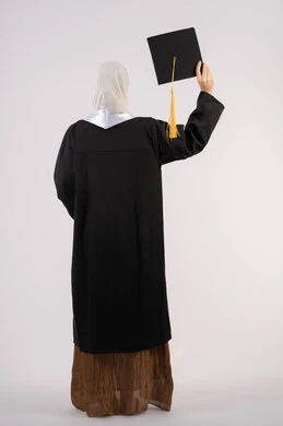 جودة التعليم في الامارات، الشعور بالفخر والفرح بالوصول لحلم التخرج, بورتريه من الخلف لخريجة عربية سعودية خليجية محجبة ترتدي عباءة وترفع قبعة التخرج، شابة إماراتية تحتفل بإنهاء دراستها الجامعية، صورة لكامل الجسم، خلفية بيضاء