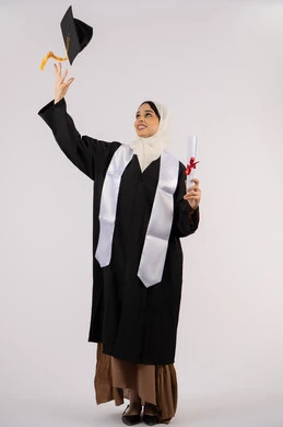 Hat toss to celebrate success and completion of university, portrait of an Arab Gulf Emirati female graduate wearing a cap and graduation gown holding a diploma in her hand, a young Saudi woman standing with expressions and gestures of pleasure and happiness, the concept of excellence and diligence, full-length body image, white background