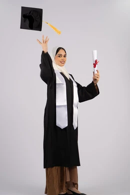 تحقيق التفوق والاجتهاد، رمي القبعة احتفالا بالنجاح وانتهاء المرحلة الجامعية، بورتريه لخريجة عربية خليجية اماراتية ترتدي قبعة وزي التخرج تمسك بيدها الشهادة، شابة سعودية تقف بتعابير وايماءات السرور والسعادة، صورة الجسم بالطول الكامل، خلفية بيضاء