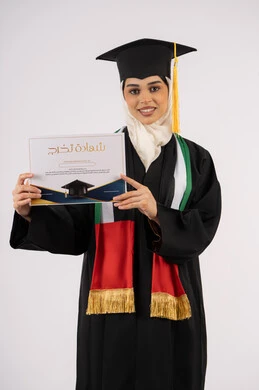 جودة التعليم في الامارات، الاحتفال بإنهاء الدراسة الجامعية، النظر الى الكاميرا بايماءات الفخر والسعادة بالوصول الى الحلم، بورتريه لخريجة عربية خليجية اماراتية محجبة ترتدي زي التخرج والقبعة تحمل بيدها شهادة التخرج، خلفية بيضاء