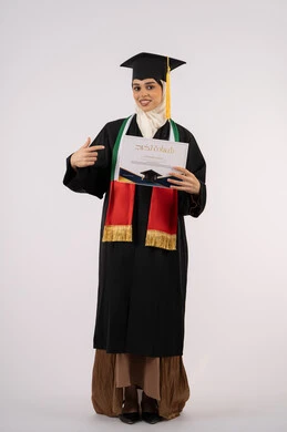 الإشارة بإصبع السبابة إلى شهادة التخرج، الاحتفال بإنهاء الدراسة الجامعية، بورتريه لخريجة عربية خليجية اماراتية محجبة ترتدي زي التخرج والقبعة تنظر الى الكاميرا بإيماءات الفخر والسعادة بالوصول الى الحلم، الجسم بالطول الكامل، خلفية بيضاء