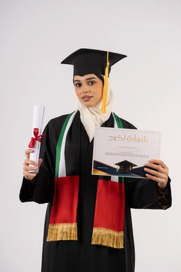 إيماءات الفخر والسعادة بالوصول الى الحلم، تحقيق الأحلام والطموحات، الاحتفال بإنهاء الدراسة الجامعية، بورتريه لخريجة عربية خليجية اماراتية محجبة ترتدي زي التخرج والقبعة تحمل وثيقة التخرج وتنظر الى الكاميرا، خلفية بيضاء