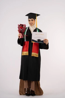 النظر إلى الكاميرا بتعابير السرور، الاحتفال بإنهاء الدراسة الجامعية، بورتريه لخريجة عربية خليجية اماراتية محجبة ترتدي زي التخرج والقبعة تمسك بيدها بوكيه ورد والشهادة بإيماءات السعادة بالوصول لحلم النجاح،، الجسم بالطول الكامل، خلفية بيضاء