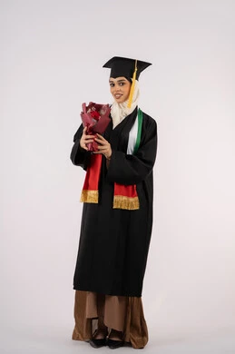 الفرح والسعادة بالوصول لحلم النجاح، بورتريه لخريجة عربية خليجية اماراتية محجبة ترتدي زي التخرج والقبعة تمسك بيدها بوكيه ورد تنظر إلى الكاميرا بتعابير السرور، الاحتفال بإنهاء الدراسة الجامعية، صورة لكامل الجسم ، خلفية بيضاء
