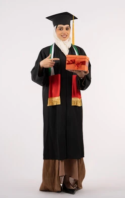 الاحتفال بإنهاء الدراسة الجامعية، تقديم الهدايا في المناسبات، إيماءات السعادة بالوصول لحلم النجاح، بورتريه لخريجة عربية خليجية اماراتية محجبة ترتدي زي التخرج والقبعة تشير بإصبع السبابة إلى صندوق الهدية، الجسم بالطول الكامل، خلفية بيضاء