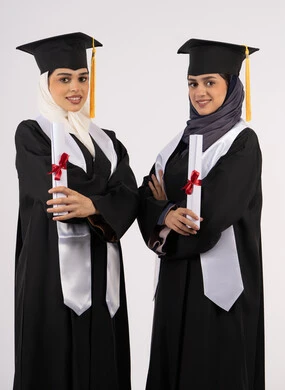 جودة التعليم في الامارات، الفرح بتحقيق الأحلام، الاحتفال مع الأصدقاء بالتخرج من الجامعة، النظر إلى الكاميرا بإيماءات السعادة والفخر، بورتريه لخريجتين جامعيتين عربيتين خليجيتين اماراتيتين ترتديان ملابس التخرج تقفان بأيدي متقاطعة وتمسكان وثيقة التفوق، خلفية بيضاء