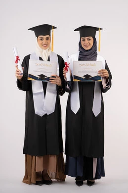 Standing up straight and looking at the camera with gestures of happiness and pride, the concept of hard work and excellence, celebrating university graduation with friends, portrait of two Arab Gulf Emirati university graduates wearing graduation clothes and holding their success certificates, full body length, white background