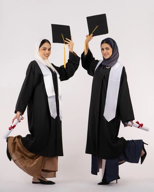 رفع قبعة التخرج للأعلى، مفهوم الاجتهاد والتفوق، النظر إلى الكاميرا بإيماءات السعادة والفخر، الاحتفال مع الأصدقاء بالتخرج من الجامعة، بورتريه لخريجتين جامعيتين عربيتين خليجيتين اماراتيتين ترتديان زي التخرج وتمسكان شهادة النجاح، طول الجسم بالكامل، خلفية بيضاء